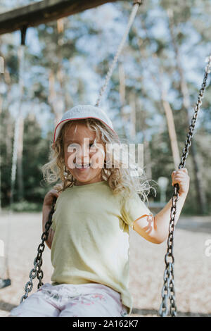 Portrait of happy girl on swing sur une aire de jeux Banque D'Images