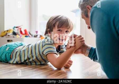 Père et fils se trouvant sur le plancher à la maison Arm wrestling Banque D'Images