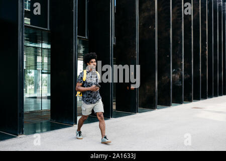 Homme avec sac à dos jaune, smartphone et écouteurs marche dans la rue, Barcelone, Espagne Banque D'Images