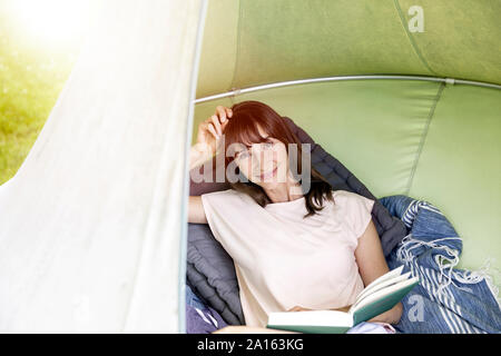 Portrait of smiling woman reading book dans une tente suspendue Banque D'Images