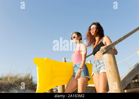 Les jeunes femmes avec matelas jaune à pied de la plage Banque D'Images