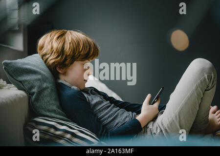 Redheaded boy lying on couch looking at cell phone Banque D'Images