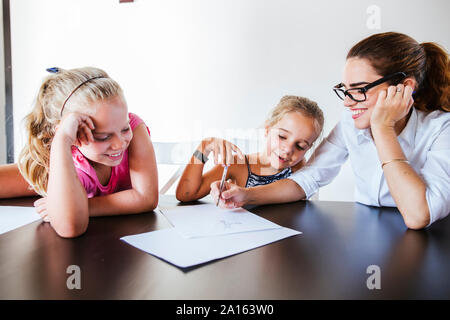 Happy teacher sitting at desk avec deux écolières écrit sur papier Banque D'Images