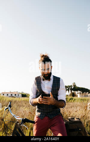 L'homme bien habillé avec son vélo dans la campagne using cell phone Banque D'Images