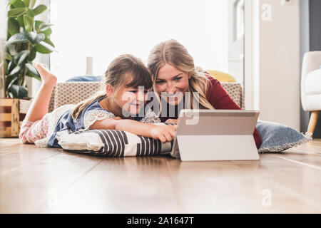 Mère et fille se trouvant sur le plancher à la maison à l'aide de tablet Banque D'Images