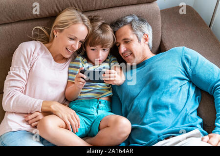 Père, mère et fils using cell phone on sofa at home Banque D'Images