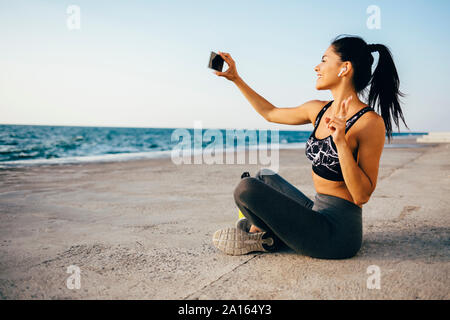 Woman using smartphone et prendre un, selfies sitting on a pier Banque D'Images