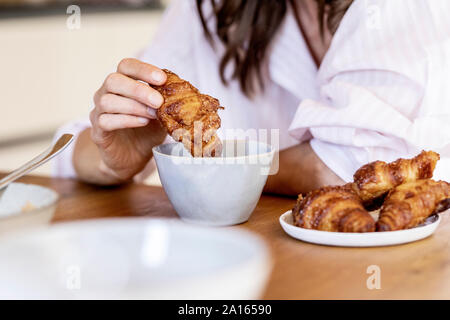 Close-up of woman trempant un croissant dans le café tasse Banque D'Images