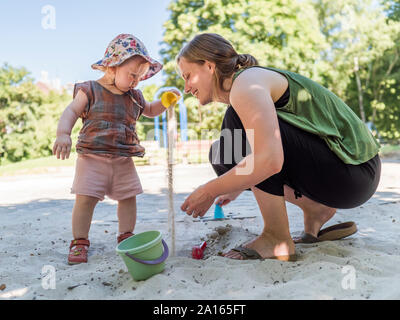 Petite fille avec sa mère dans sandbox sur aire Banque D'Images