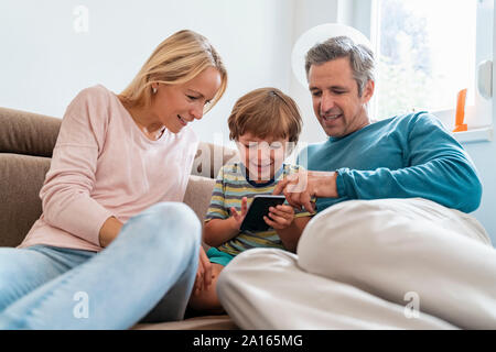 Père, mère et fils using cell phone on sofa at home Banque D'Images