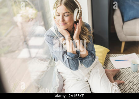 Femme assise à la fenêtre à la maison écouter de la musique avec des écouteurs Banque D'Images