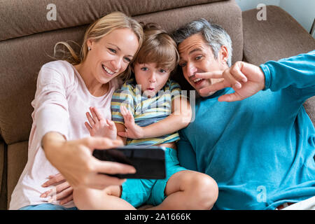 Père, mère et fils en tenant une table à la maison sur selfies Banque D'Images