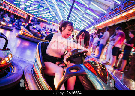 Deux jeunes femmes équitation voiture bumbper sur une fête foraine la nuit Banque D'Images