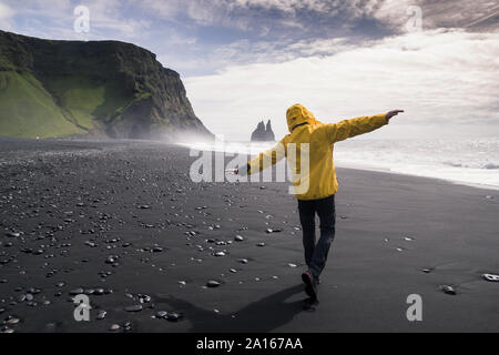 Man marche sur une plage de lave en Islande, with arms outstretched Banque D'Images