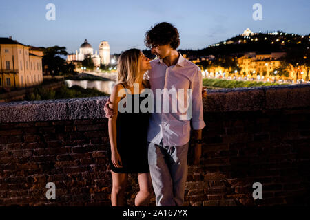 Jeune couple dans l'amour embrassant sur un pont la nuit, Vérone, Italie Banque D'Images