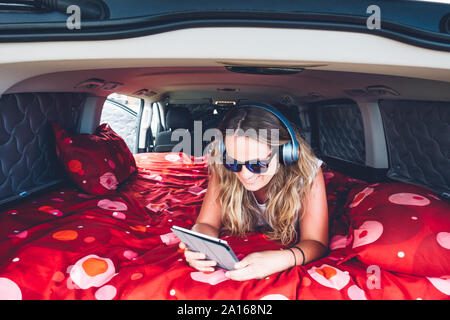 Jolie femme blonde avec des lunettes et des écouteurs en camping à l'intérieur d'un van à l'aide de tablet Banque D'Images