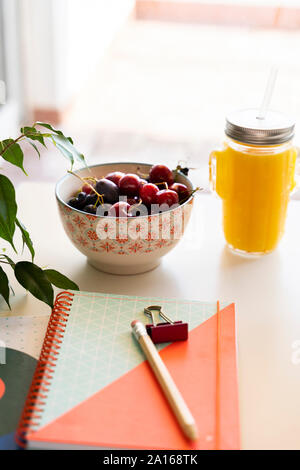 Smoothie orange et le bol de cerises sur la table avec un ordinateur portable et crayon Banque D'Images