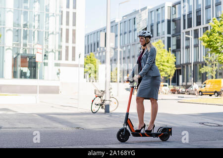Smiling businesswoman wearing High heels riding scooter électrique sur la rue Banque D'Images