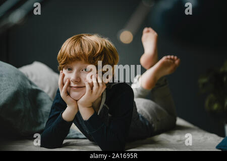 Portrait of smiling redheaded garçon couché sur la table à la maison Banque D'Images