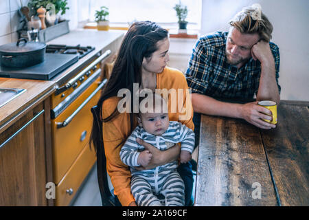 Famille sérieuse avec bébé assis à table de cuisine à la maison Banque D'Images