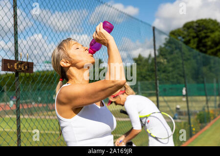 Femme mature tennis club à prendre une pause pour jouer à partir de l'eau potable bouteille Banque D'Images