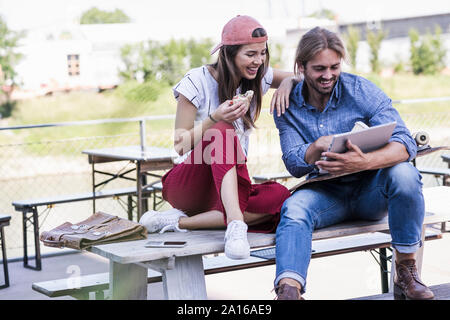 Young couple sitting on table dans un café en plein air à l'aide de tablet Banque D'Images