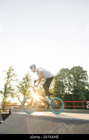 Jeune homme équitation vélo BMX au skatepark au coucher du soleil Banque D'Images