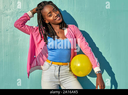 Jeune femme noire avec une balle jaune devant un mur bleu Banque D'Images