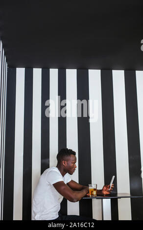 Jeune homme assis à table avec un verre à l'aide de téléphone cellulaire Banque D'Images