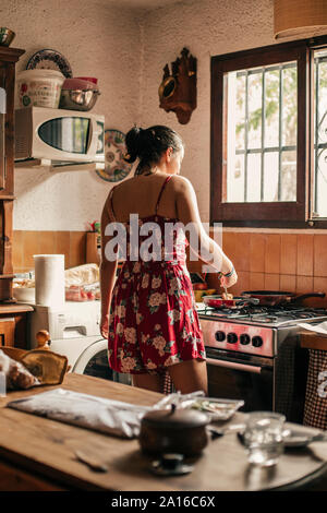 Vue arrière du woman cooking in kitchen en utilisant une casserole Banque D'Images