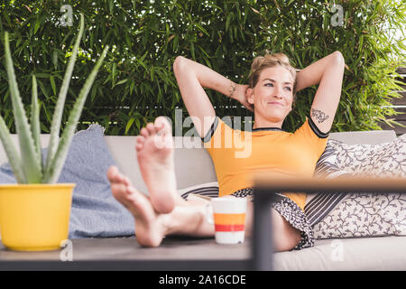 Relaxed woman sitting on couch sur terrasse à la maison en se penchant en arrière Banque D'Images