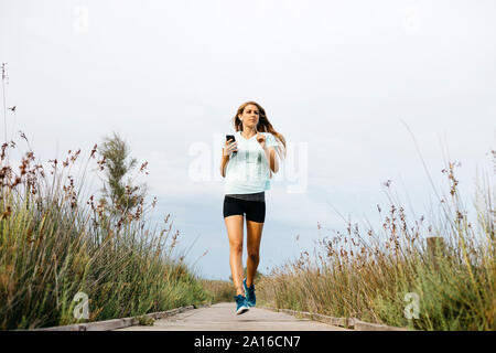Female jogger running on allée en bois, écouter de la musique Banque D'Images