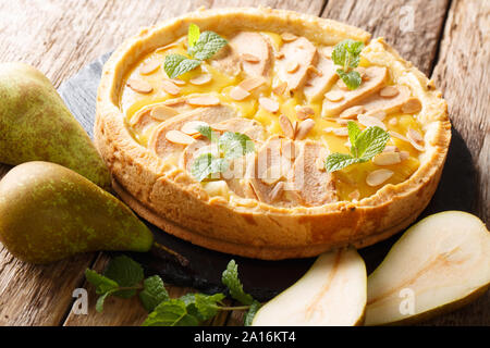 Tarte aux poires fraîches faites maison avec de la crème anglaise, les amandes et la menthe libre sur une liste de sélection sur une table horizontale. Banque D'Images