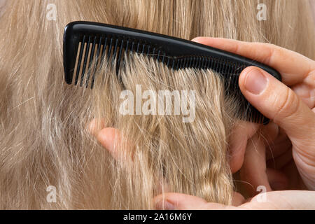 Main de coiffure le peignage des cheveux blonds, closeup Banque D'Images