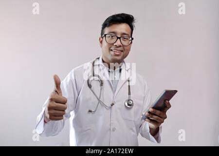 Femme médecin indien en blouse blanche et stéthoscope showing Thumbs up avec smart phone Banque D'Images