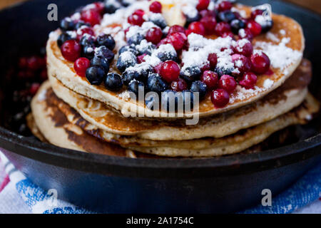 Pile de crêpes à l'avoine fait maison, les bleuets et le sucre powered airelles rouges mouillees dans poêle en fonte sur la table rustique de pays. Soft focus. Copier l'espace. Absolution Banque D'Images