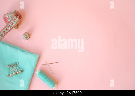 Accessoires de couture, tissu turquoise sur fond rose. Tissu, pins, fils et aiguilles. Banque D'Images