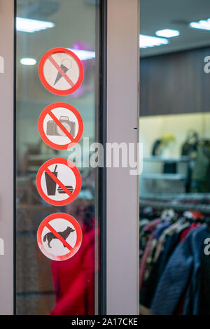 Les panneaux d'interdiction, près de l'entrée de la boutique de vêtements. Autocollants sur la vitre de fenêtre, près de la porte avec l'interdiction. Dans les cercles rouges, des icônes avec sy Banque D'Images