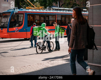 Moscou, Russie - le 14 septembre 2019 : deux courriers en uniforme vert de marque et le club livraison Sacs à communiquer à côté d'un arrêt de tramway. Sac thermique wi Banque D'Images