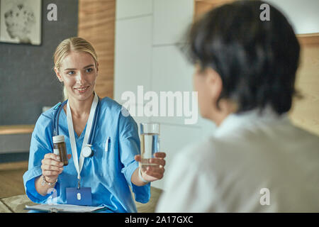 Beautiful smiling woman le médecin dans une bouteille de pilule n'offre le patient. Une panacée ou de sauvetage d'un antidépresseur prescrit boutique juridique vitam Banque D'Images