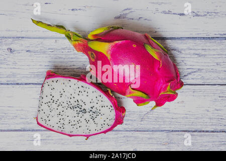 Fruit du dragon à côté d'un demi-dragon fruit rose sur fond de bois blanc Banque D'Images