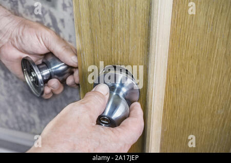 L'installation de la porte, la poignée de porte s'installe, la menuiserie mains libre. Handyman installe une nouvelle serrure de porte dans la chambre. Banque D'Images