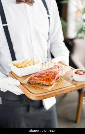 Le serveur est maintenant une plaque de bois des côtes de porc délicieux. BBQ côtelettes de porc sur la plaque en bois avec frites et salade Banque D'Images