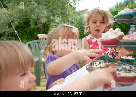 Trois jeunes filles atteignant pour cupcakes Banque D'Images