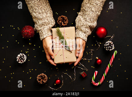 Cadeaux d'artisanat de Noël avec des rubans rouges, des pommes de pin et des décorations d'or et rouge sur fond noir. Don de femmes. Banque D'Images