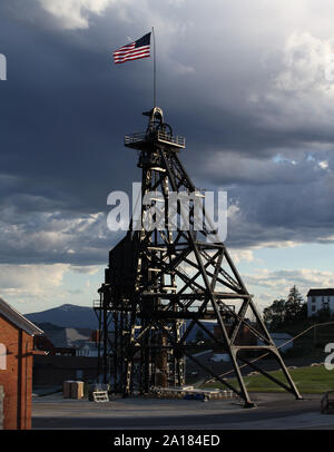 Storm clouds roll vers un chevalement surmontée d'un drapeau américain en Butte, Montana. Banque D'Images