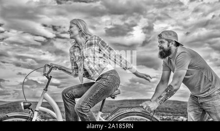 Vélo fille tandis que l'homme la soutenir. Aide à croire en vous-même. Impulsion L'impression de commencer à bouger. Des promenades en vélo femme fond de ciel. Pousser et la promotion. Impulsion à se déplacer. Homme pousse fille faire du vélo. Banque D'Images