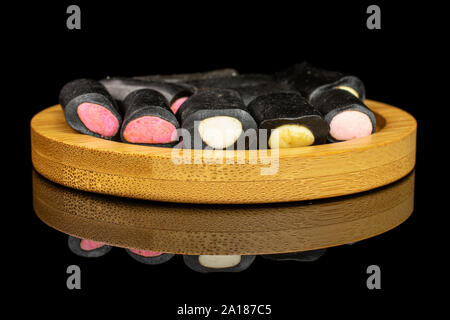 Ensemble beaucoup de bonbon à la réglisse noire sucrée sur coaster bambou isolé sur verre noir Banque D'Images