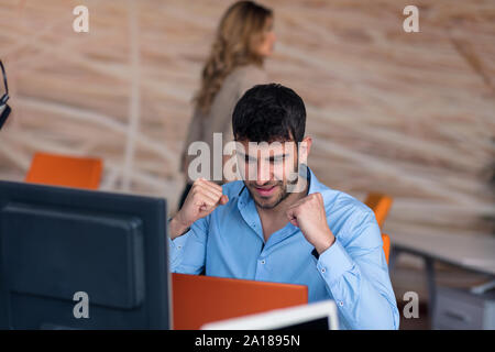 Vue de côté. Young businessman wearing blue shirt barbu,assis à table et à l'aide d'ordinateur portable. Freelancer vérification du courrier électronique. Banque D'Images