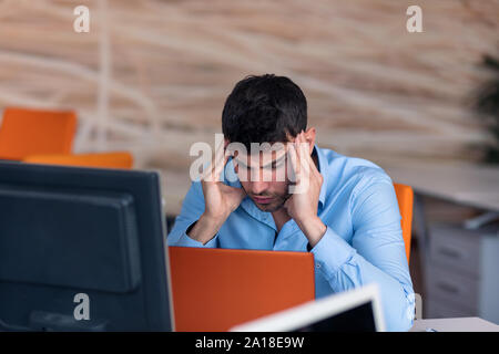 Vue de côté. Young businessman wearing blue shirt barbu,assis à table et à l'aide d'ordinateur portable. Freelancer vérification du courrier électronique. Banque D'Images